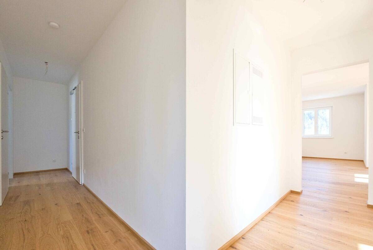 Heller Flur mit Holzboden und weißen Wänden, der zu verschiedenen Räumen führt.