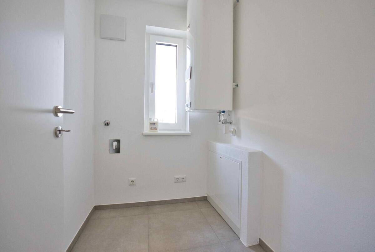 Praktischer Hauswirtschaftsraum mit Fenster, Fliesenboden und Anschlüssen für Geräte.