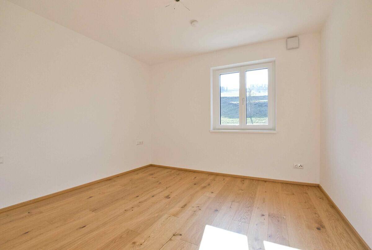 Unmöbliertes Schlafzimmer mit hellem Holzboden, weiß gestrichenen Wänden und einem Fenster.
