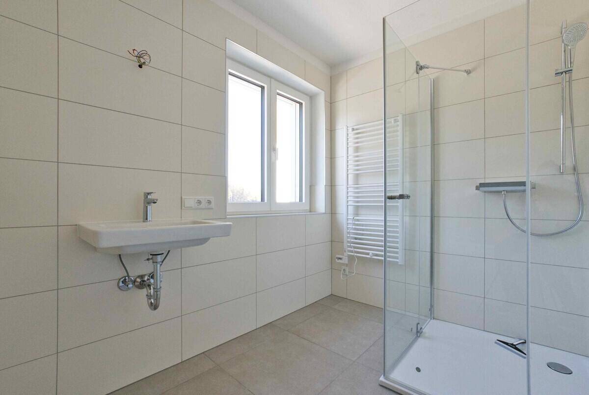 Modernes Badezimmer mit ebenerdiger Dusche, Waschbecken, Handtuchheizkörper und Fenster.