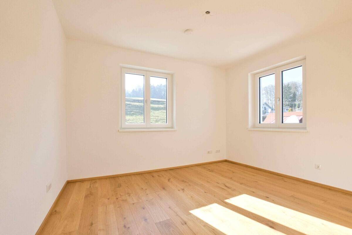 Helles Schlafzimmer mit zwei Fenstern, Holzboden und weiß gestrichenen Wänden, unmöbliert.