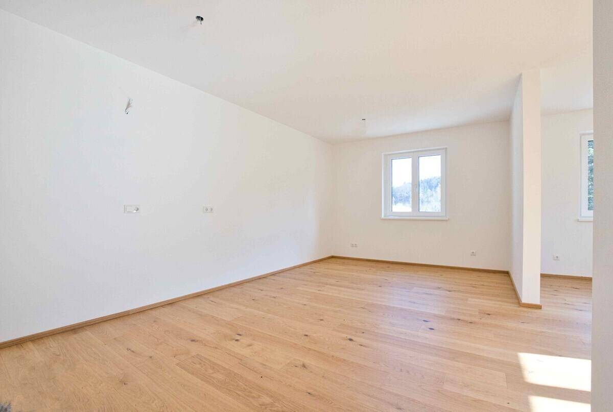 Geräumiger, unmöblierter Wohnbereich mit hellem Holzboden und weiß gestrichenen Wänden.