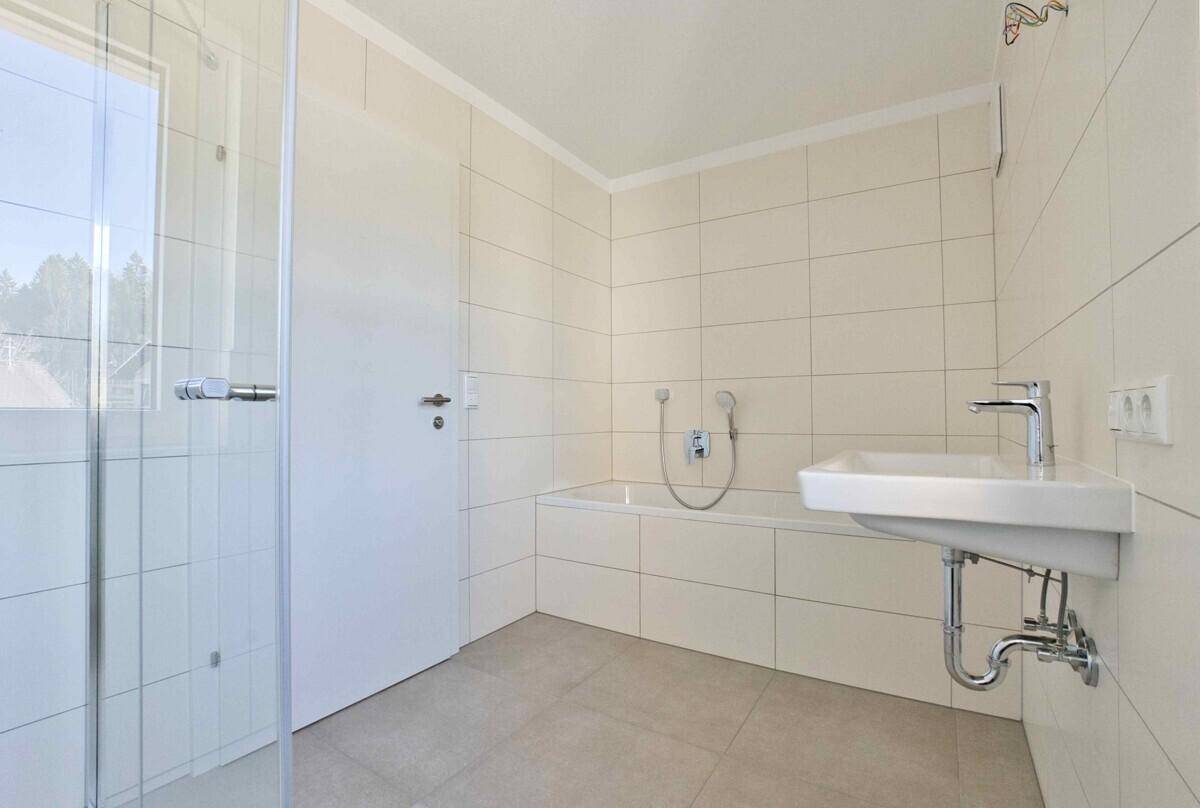 Helles Badezimmer mit Badewanne, Waschbecken und moderner Duschkabine, gefliest.