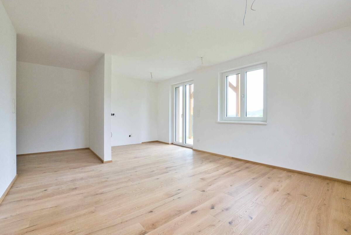 Helles, unmöbliertes Zimmer mit Holzboden und Zugang zu einem Außenbereich.