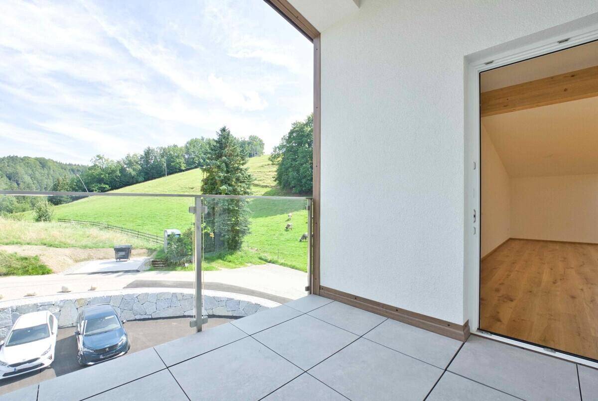 Balkon mit Fliesenboden und Glasgeländer, bietet einen weiten Blick auf grüne Hügel und Natur.