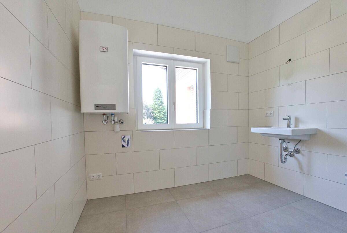 Funktionaler Raum mit weißen Fliesen, Waschbecken und Warmwasserbereiter, ideal als Hauswirtschaftsraum.