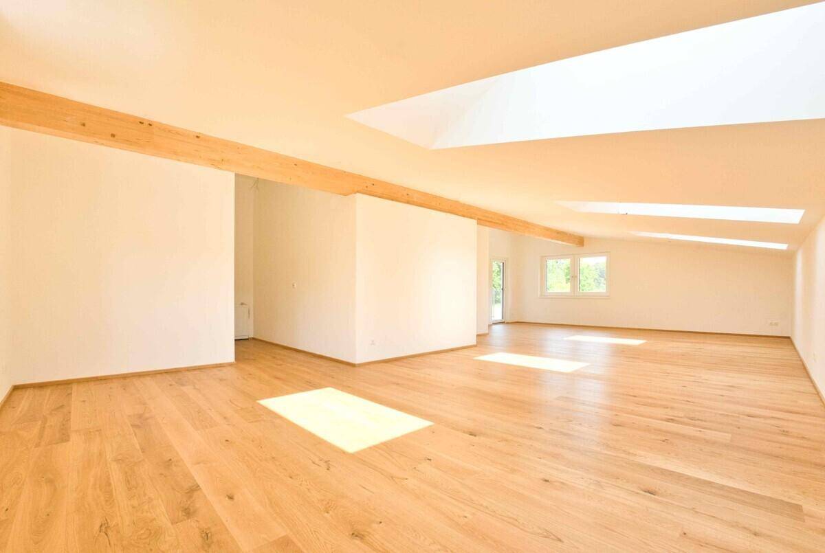Lichtdurchfluteter Raum mit Holzbalken, Parkettboden und großen Dachfenstern, bereit zum Einzug.