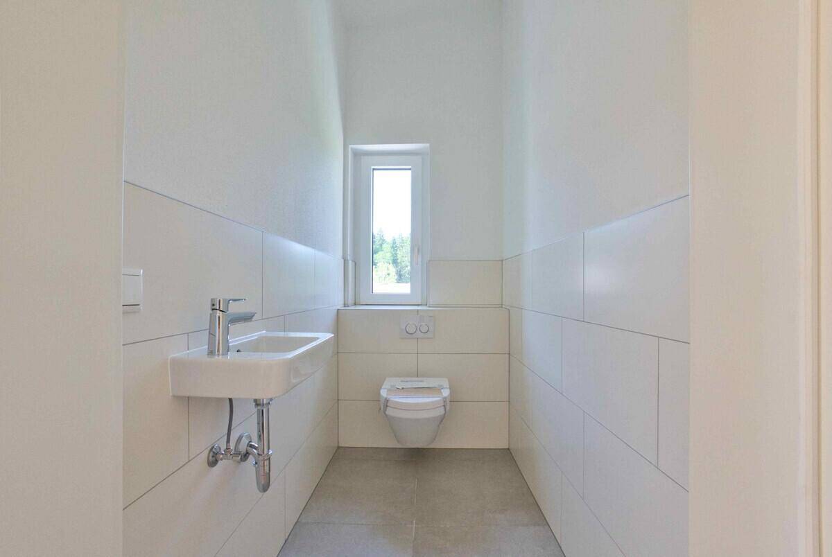 Helles Gäste-WC mit wandhängender Toilette und kleinem Waschbecken, modern gefliest.
