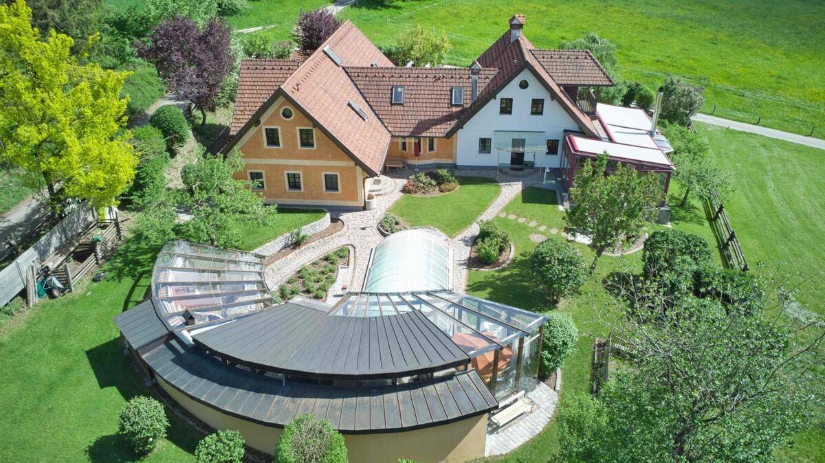 Vogelperspektive des Anwesens mit großem Garten, überdachtem Pool und weitläufigen Grünflächen.