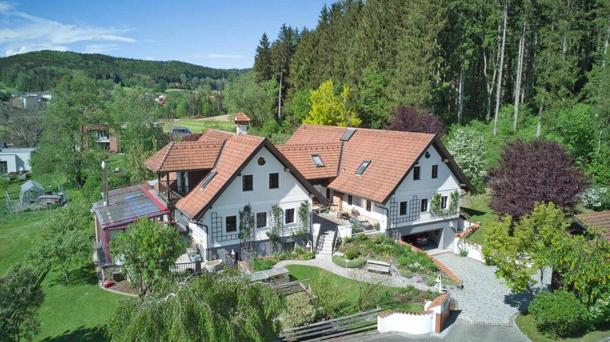 Panoramablick auf das Anwesen mit weitläufigem Garten, Zufahrt und angrenzendem Waldgebiet.