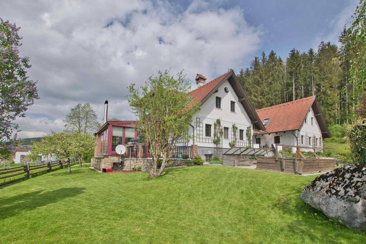 Seitenansicht des Hauses vom weitläufigen Garten aus mit Rasenflächen und angrenzendem Wald.