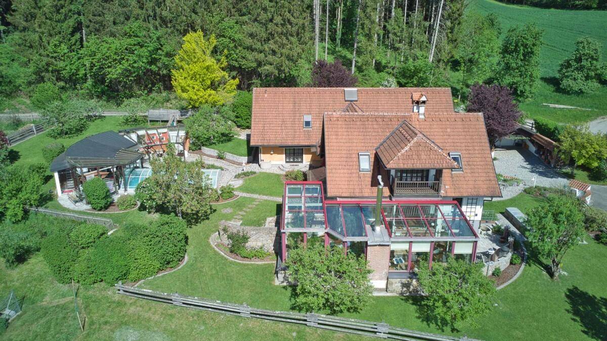Rückansicht des Hauses mit großem Wintergarten, überdachtem Pool und weitläufigem Gartenbereich.