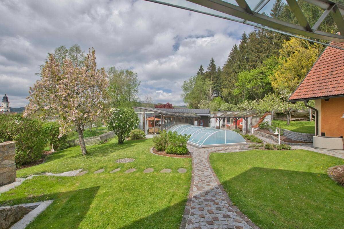 Gepflegter Gartenbereich mit Steinweg, blühenden Bäumen und dem überdachten Pool im Hintergrund.