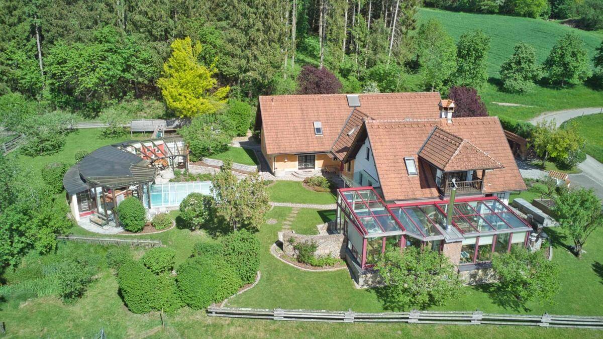 Luftaufnahme der Rückseite des Hauses mit Wintergarten, überdachtem Pool und weitläufigem Garten.