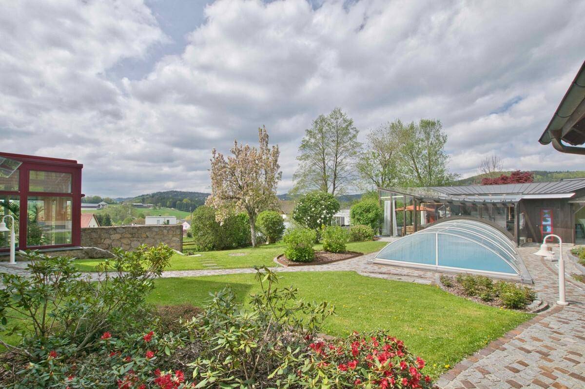 Weitläufiger Garten mit überdachtem Pool, gepflegten Beeten und Panoramablick auf die Umgebung.
