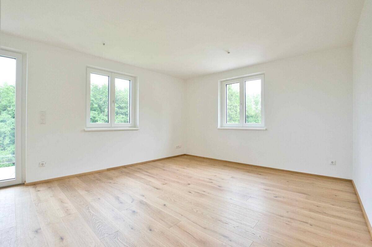 Helles, leeres Zimmer mit Holzboden und Fenstern mit Blick ins Grüne, bereit zur Gestaltung.