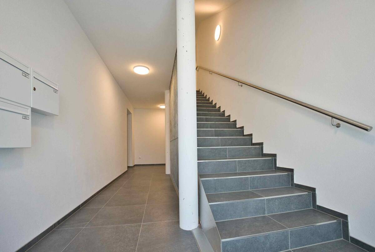 Heller Treppenaufgang mit Fliesenboden und Handlauf, führt zu den oberen Etagen des Gebäudes.