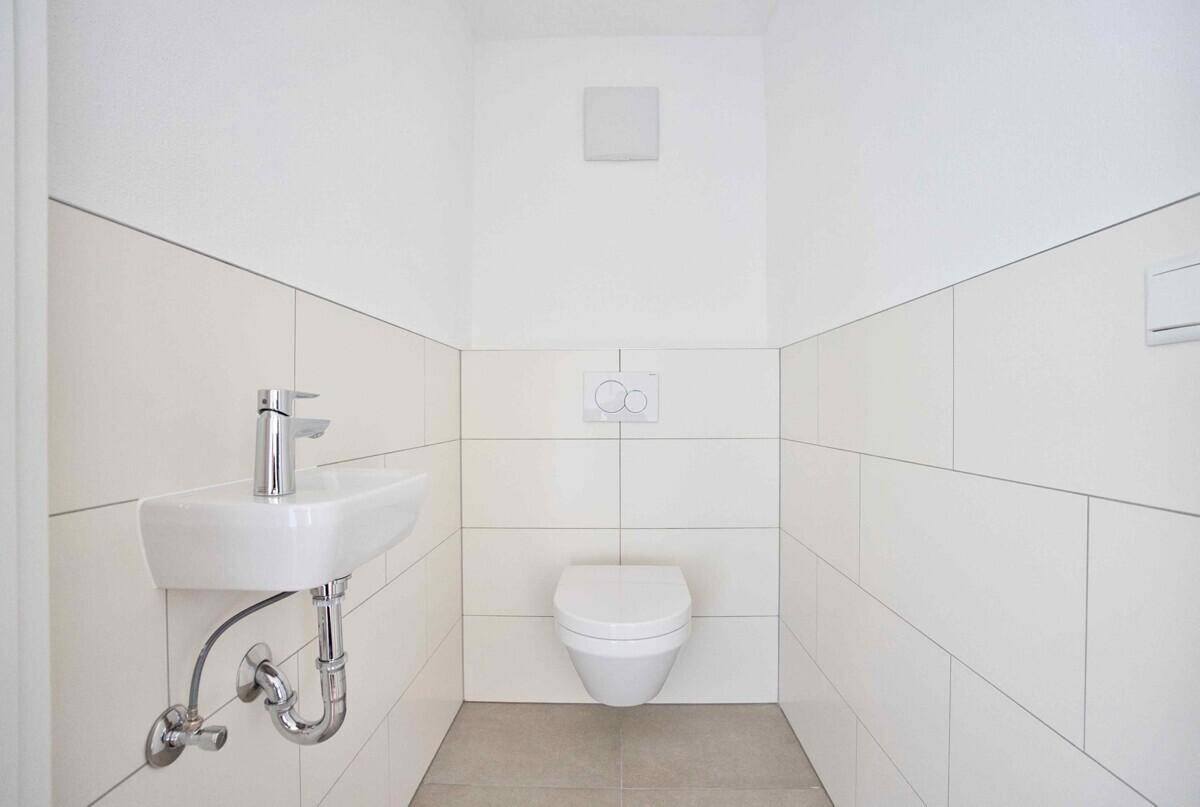 Kleines, modernes Gäste-WC mit wandhängender Toilette und Waschbecken, hell gefliest.