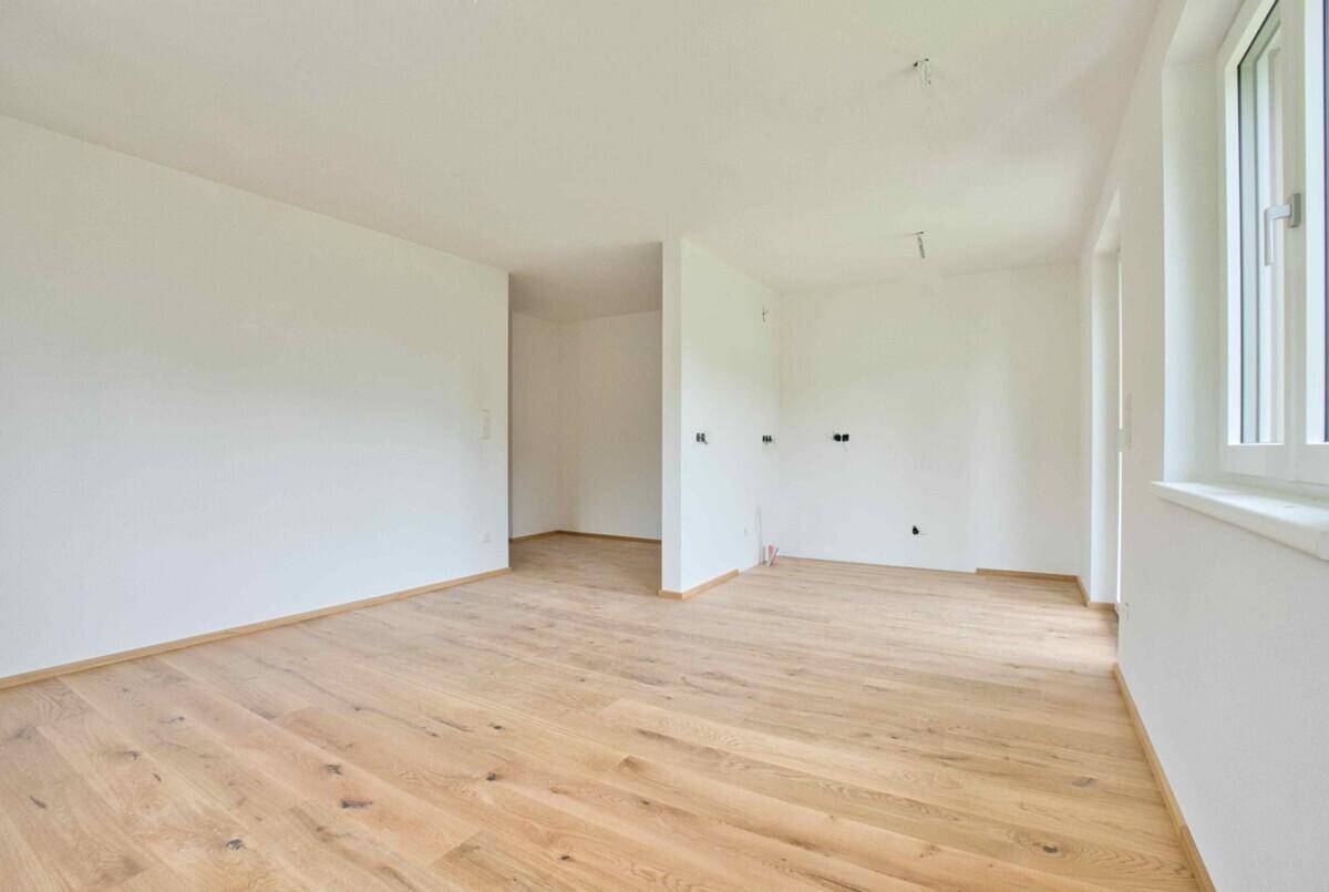 Geräumiges, helles Zimmer mit Holzboden und weiß gestrichenen Wänden, ideal für offenes Wohnen.