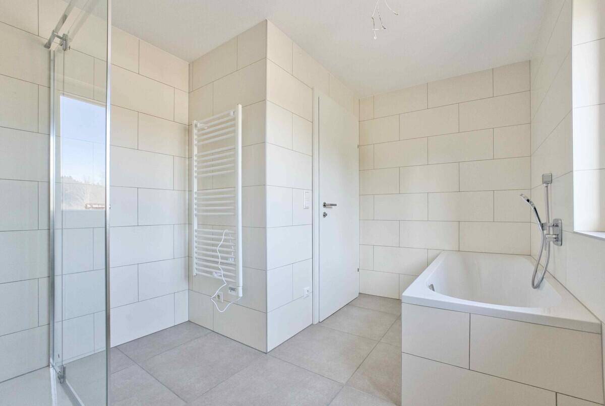 Geräumiges Badezimmer mit Badewanne, Dusche und beheiztem Handtuchhalter, in hellen Tönen gehalten.