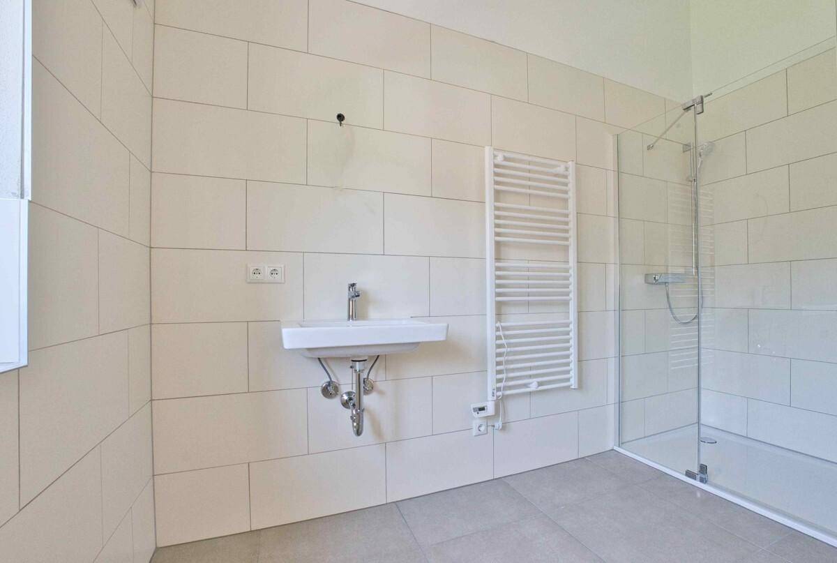 Helles Badezimmer mit Dusche, Waschbecken und beheiztem Handtuchhalter, modern gefliest.