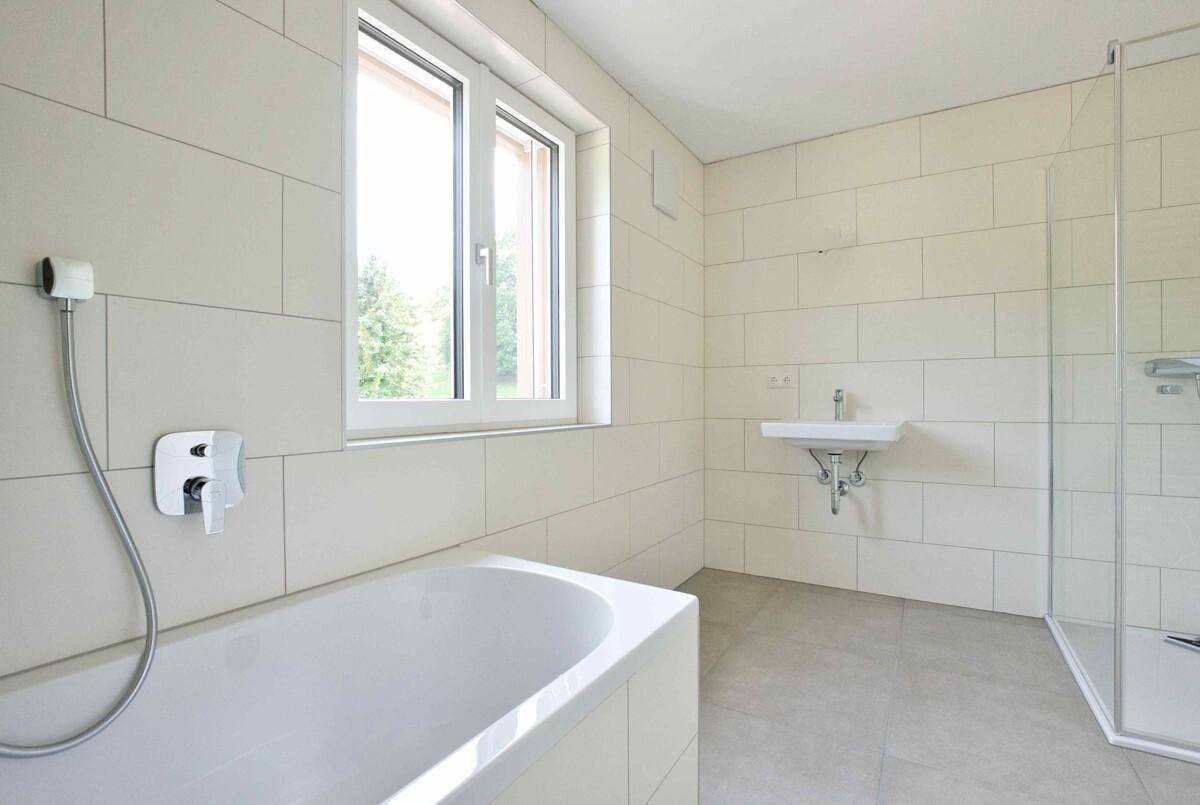 Modernes Badezimmer mit Badewanne, Dusche und Fenster, hell gefliest und gut beleuchtet.