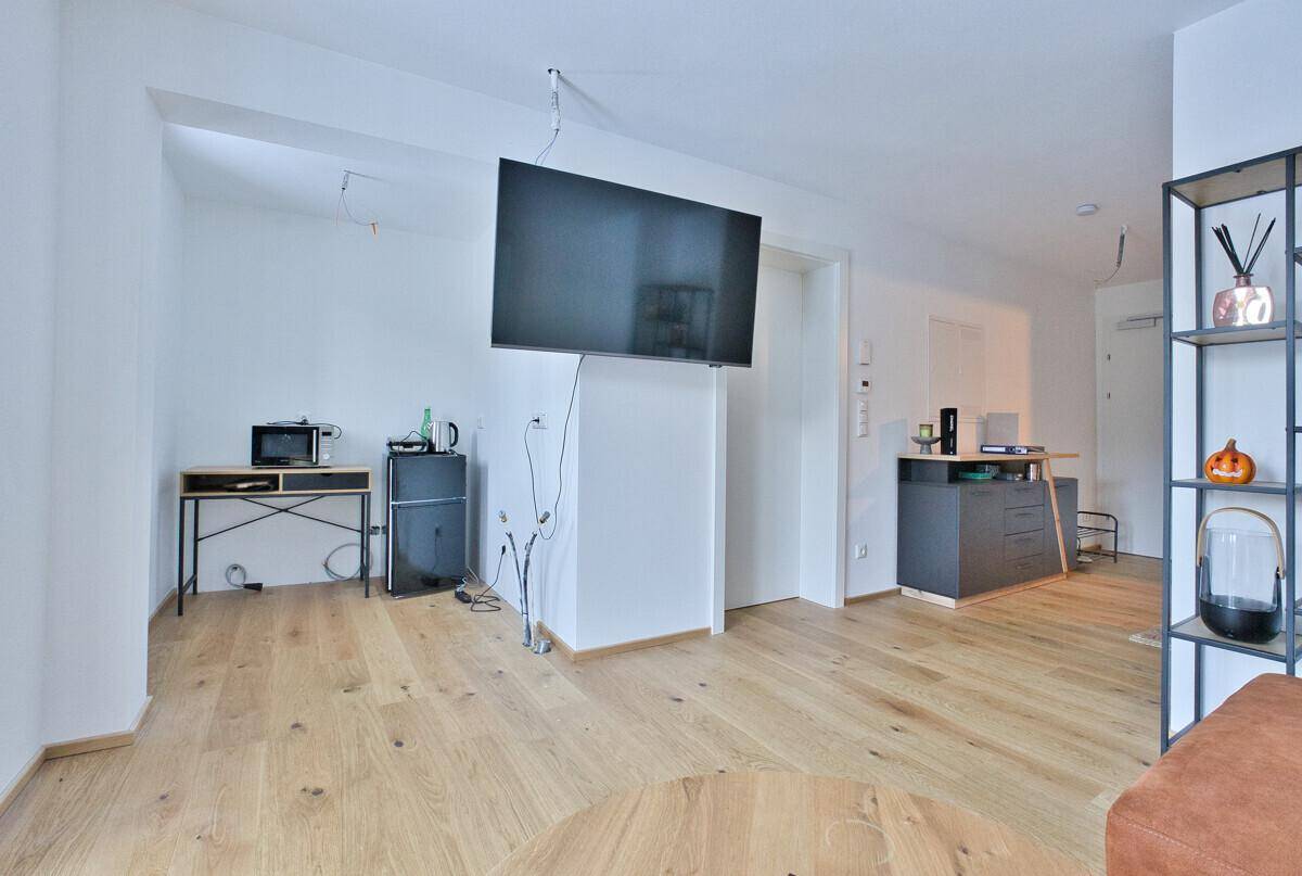 Offener Wohnbereich mit Wandfernseher, Holzboden und moderner Einrichtung.