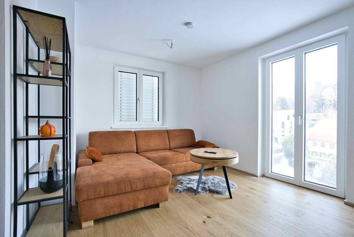 Helles Wohnzimmer mit modernem Sofa, Holzboden und großem Fenster für viel Tageslicht.