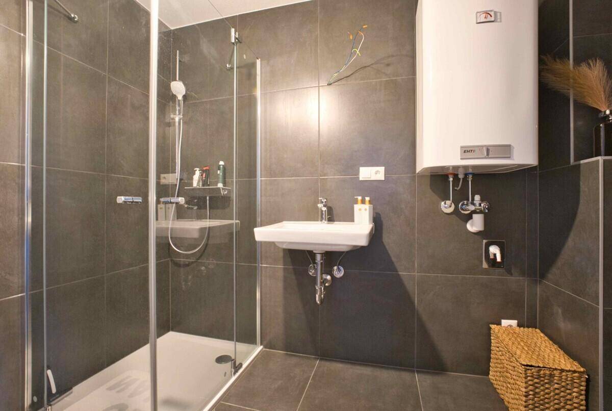 Modernes Badezimmer mit begehbarer Dusche, dunkelgrauen Fliesen und wandhängendem WC.