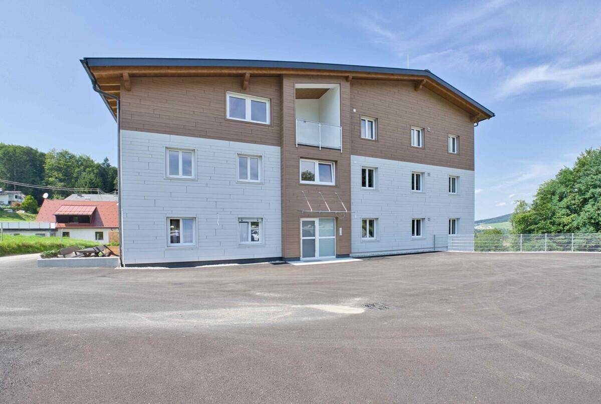 Neubau-Fassade mit modernen Balkonen und Holzverkleidung, umgeben von Natur.