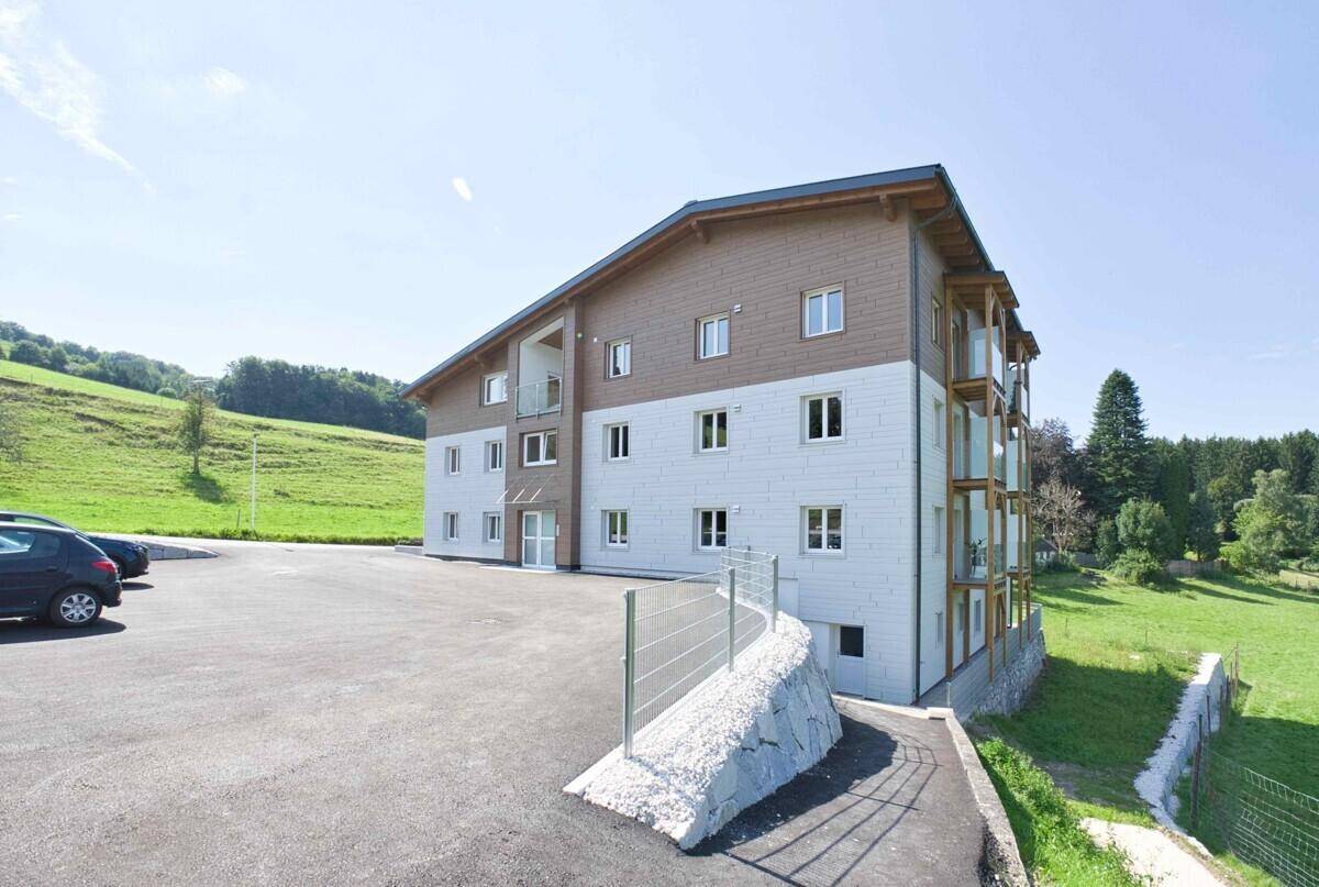 Modernes Wohngebäude in ländlicher Umgebung mit Parkplätzen und Blick auf grüne Hügel.