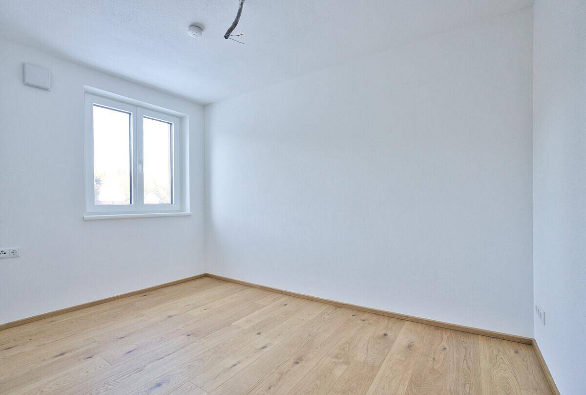 Leeres Schlafzimmer mit hellem Holzboden und großem Fenster für natürliches Licht.