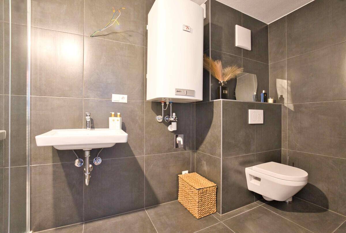 Modernes Badezimmer mit dunkelgrauen Fliesen, wandhängendem WC und Einzelwaschbecken.