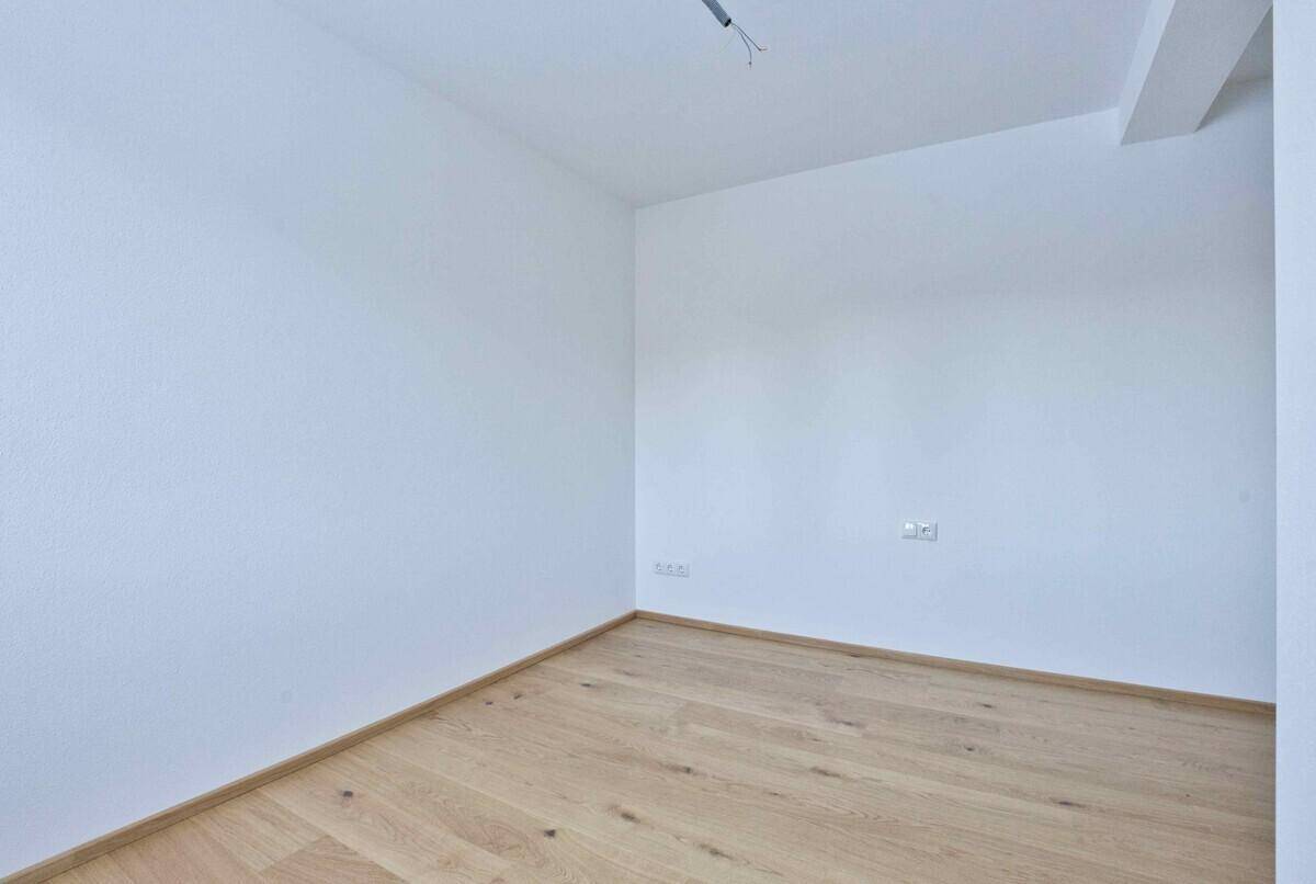 Geräumiges Zimmer mit hellem Holzboden und weißen Wänden, ideal für Schlaf- oder Arbeitsbereich.