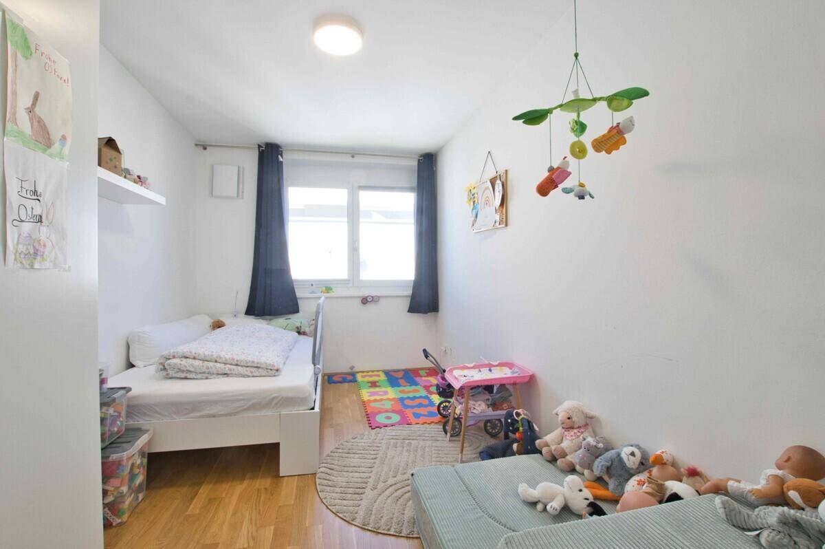 Freundliches Kinderzimmer mit Einzelbett, Spielteppich und vielen Spielsachen.