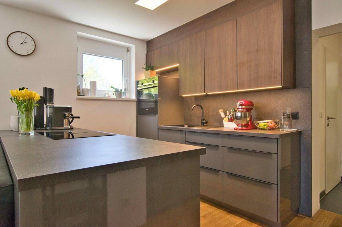 Moderne Einbauküche mit dunklen Fronten, integriertem Backofen und Kochinsel mit Spüle.