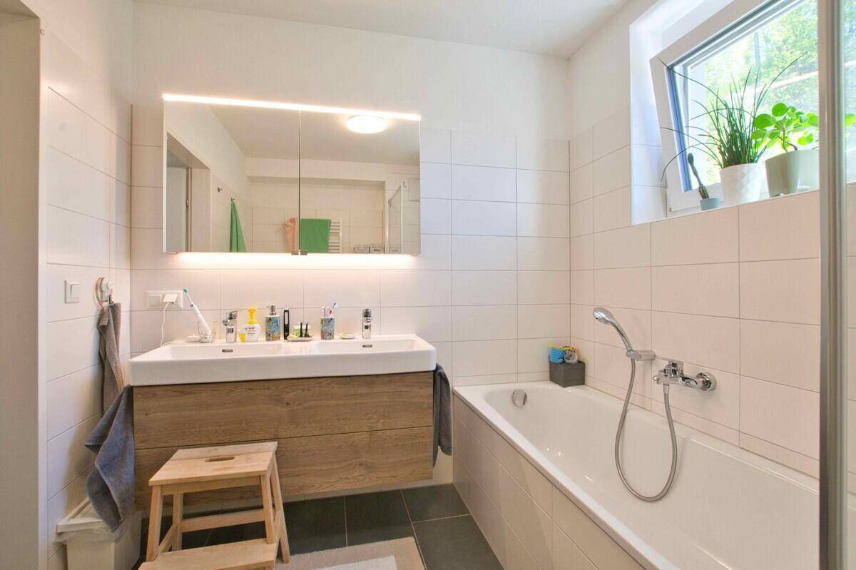 Modernes Badezimmer mit Badewanne, Doppelwaschbecken und Spiegelschrank, hell durch Fenster.