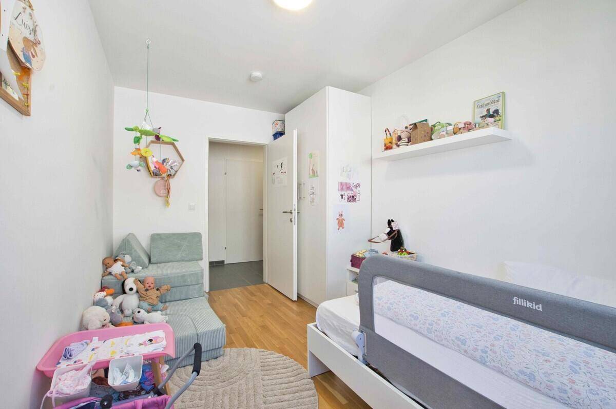 Helles Kinderzimmer mit Bett, Spielzeug und Zugang zum Flur, ideal für kleine Bewohner.
