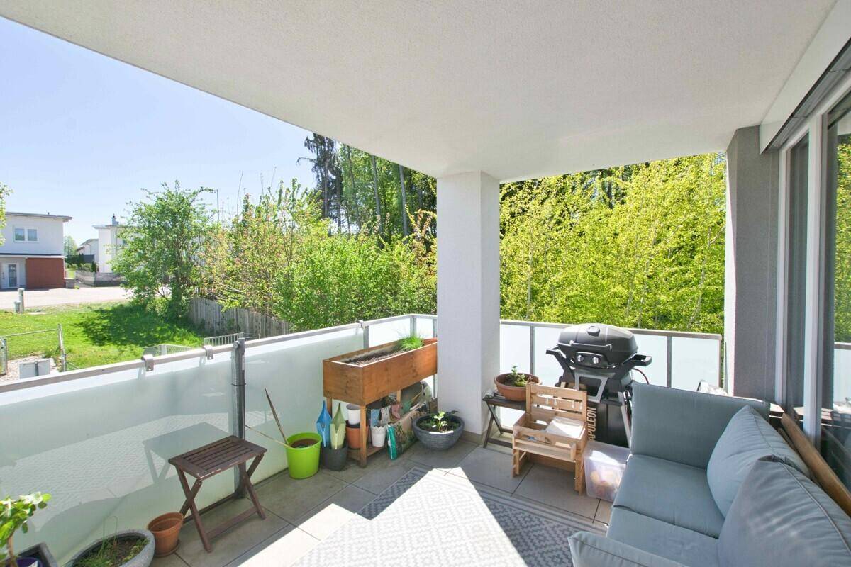 Sonniger Balkon mit Sitzgelegenheiten, Grill und Pflanzen, umgeben von viel Grün.