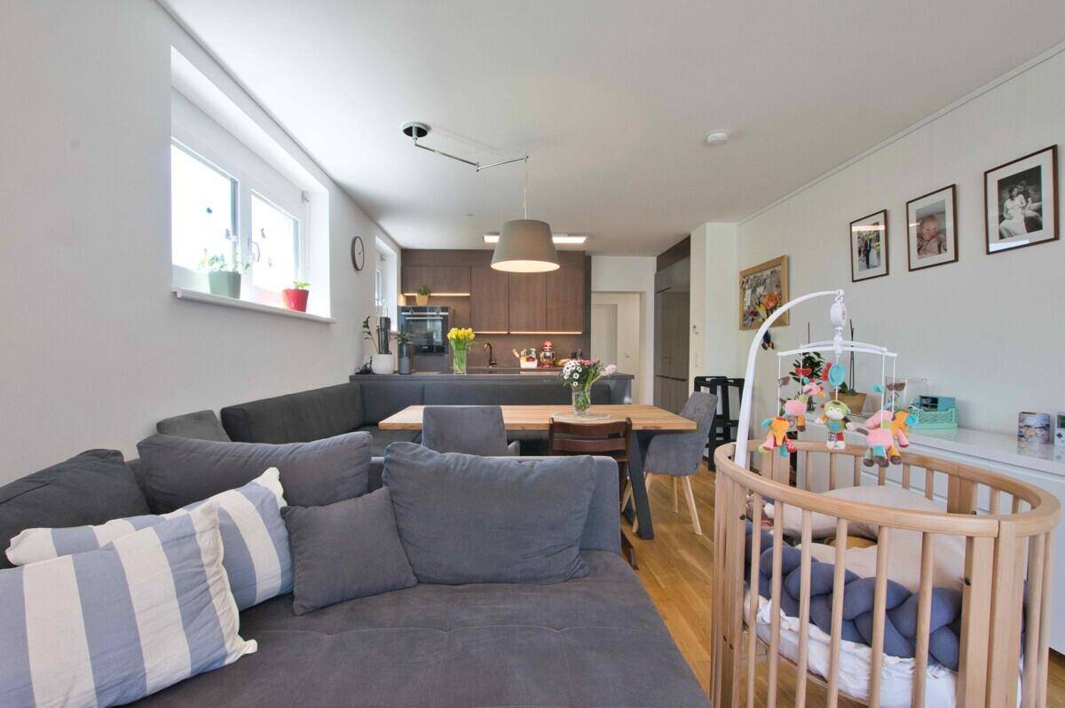 Gemütlicher Wohnbereich mit großem Sofa und Babybett, offen zur modernen Küche gestaltet.