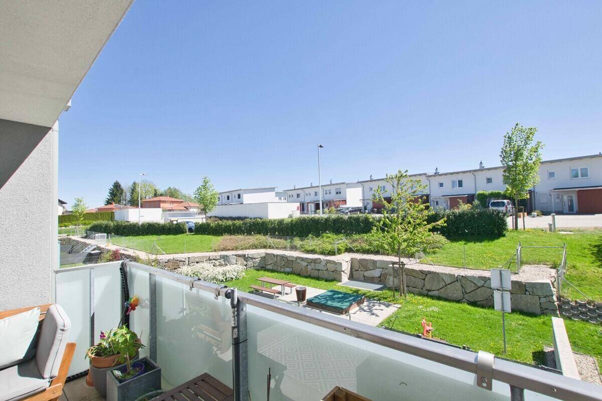 Balkon mit weitem Blick über die gepflegte Gemeinschaftsgrünfläche und umliegende Häuser.