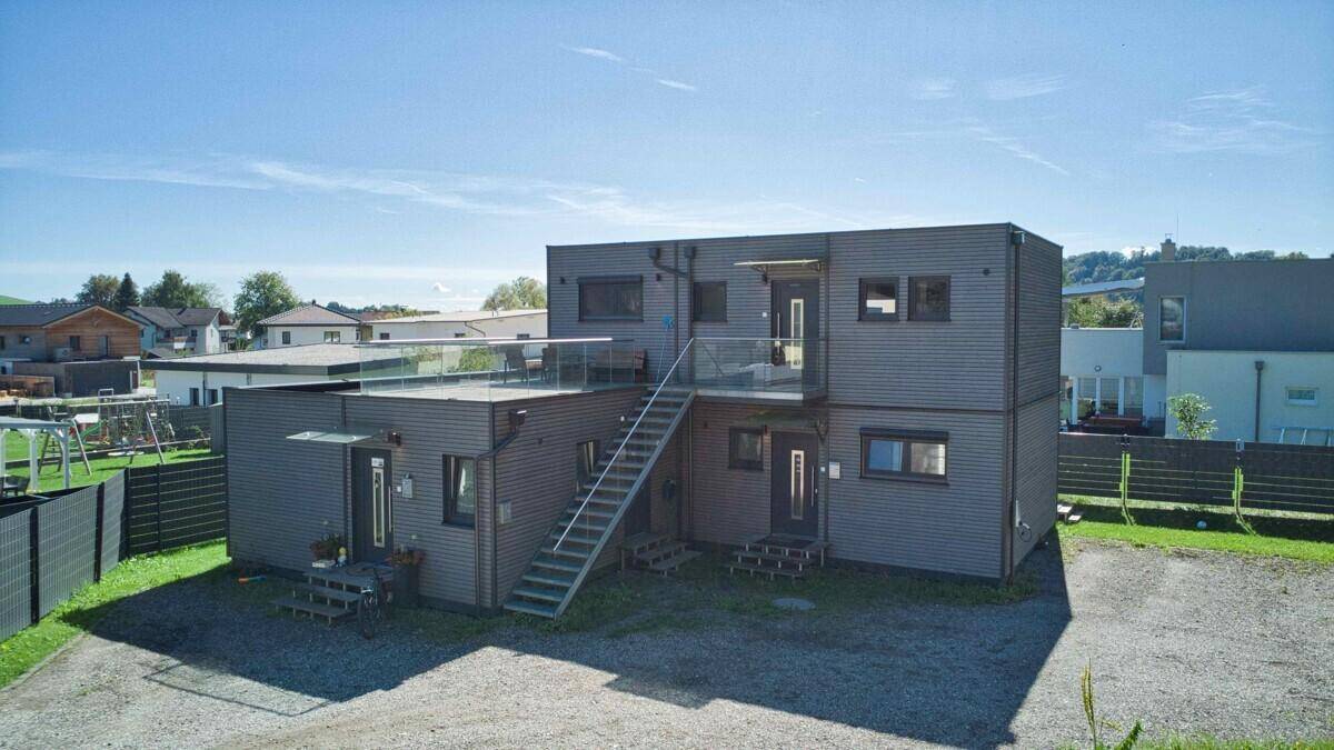 Moderne zweistöckige Wohnanlage mit Außentreppe und Dachterrasse, umgeben von einer Kiesfläche.