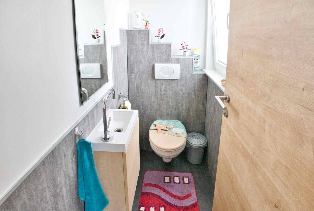 Separates WC mit Toilette, kleinem Waschbecken und Fenster, freundlich dekoriert.