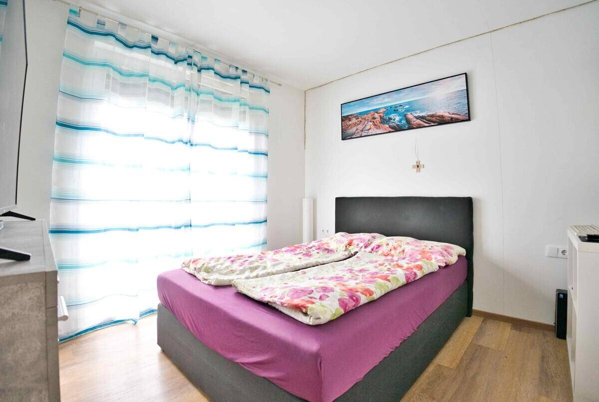 Schlafzimmer mit Doppelbett, farbenfroher Bettwäsche und Fenster mit Vorhängen.