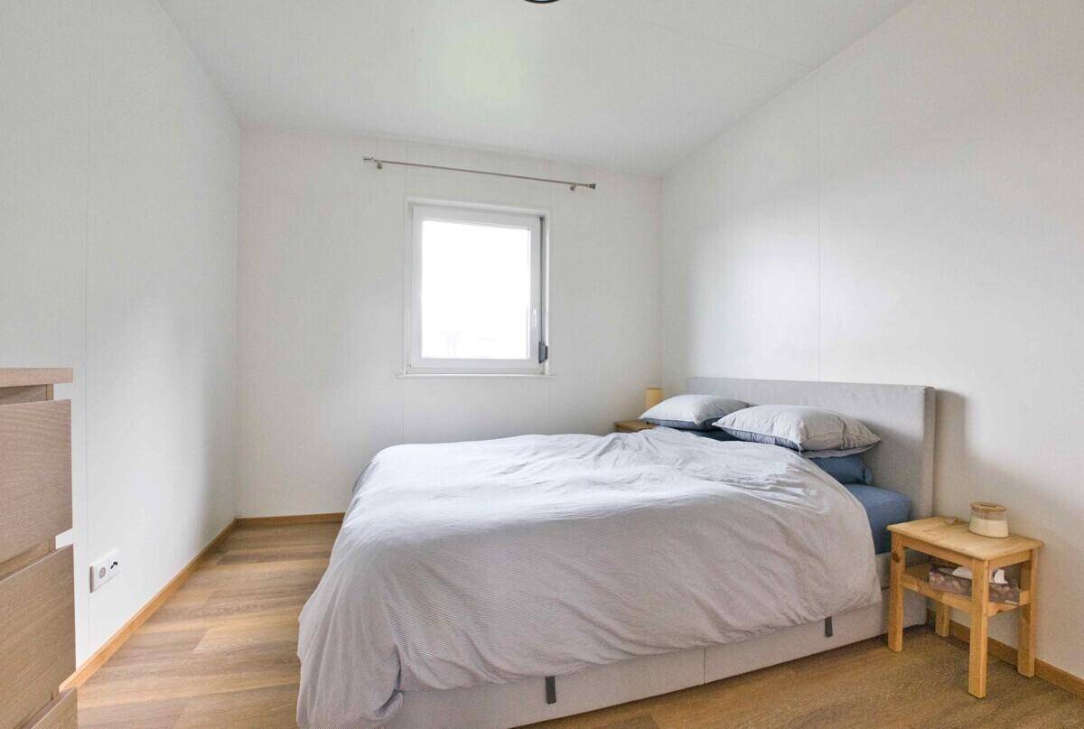 Helles Schlafzimmer mit Doppelbett, schlichten weißen Wänden und Holzboden.