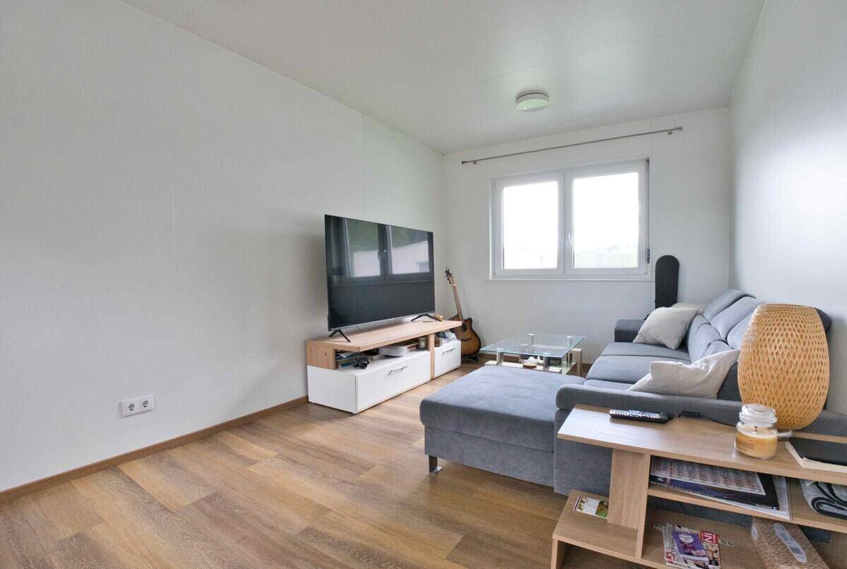 Helles Wohnzimmer mit modernem Sofa, Fernseher und hellem Holzfußboden.
