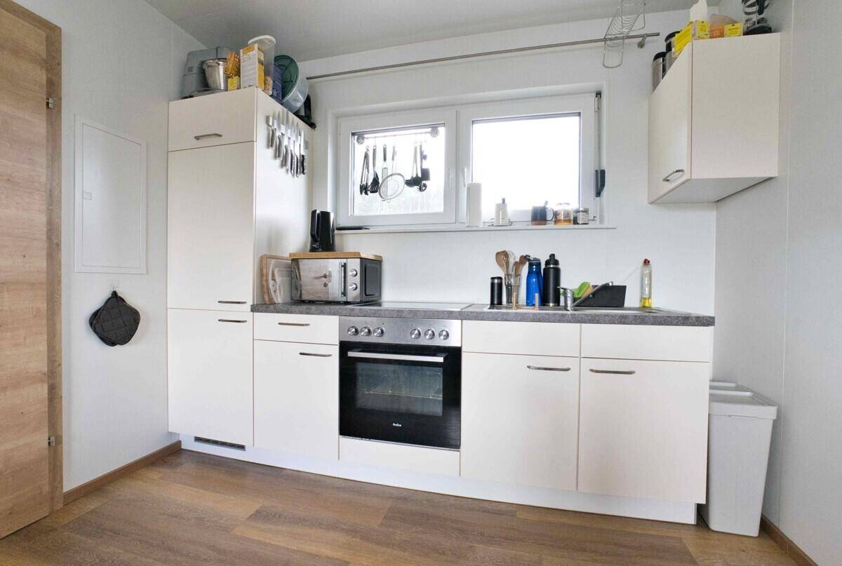 Funktionale Küchenzeile mit weißen Schränken, Backofen und Fenster für Tageslicht.
