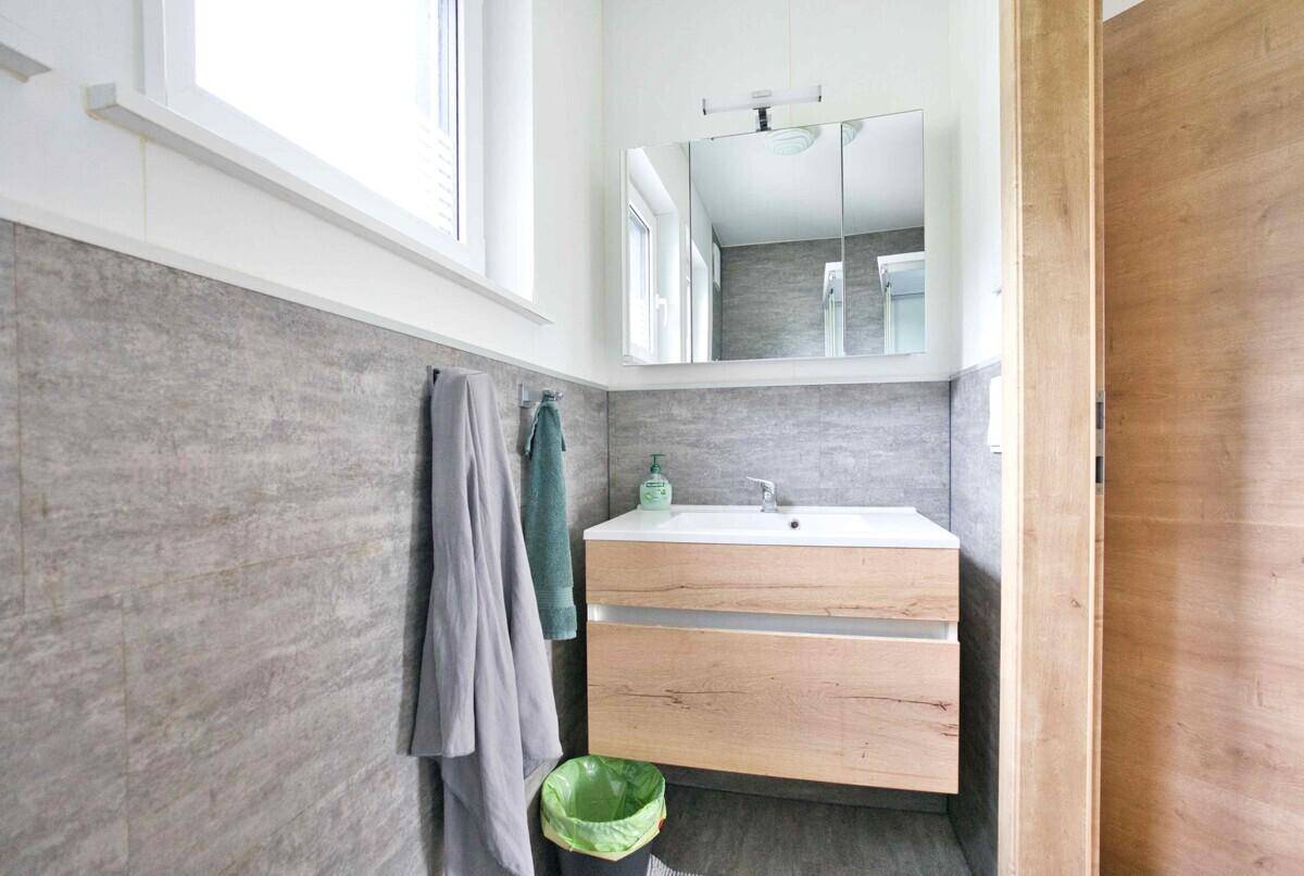 Badezimmer mit modernem Waschtisch, Spiegelschrank und Fenster für natürliche Belichtung.