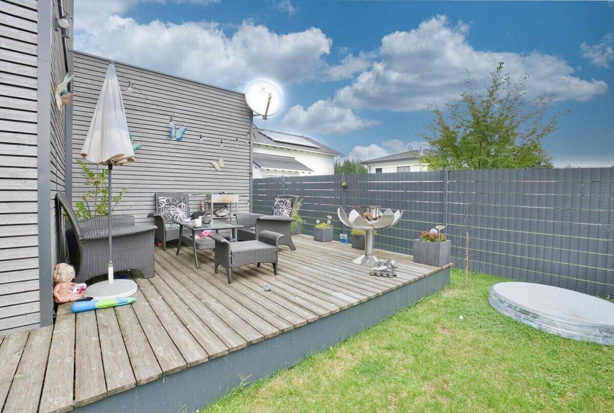 Geräumige Holzterrasse mit Gartenmöbeln und Grillbereich, umgeben von einer gepflegten Rasenfläche.