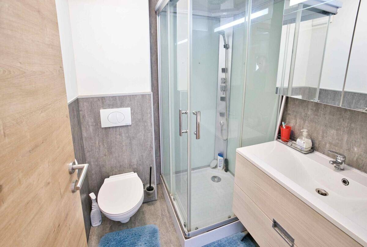 Badezimmer mit Duschkabine, Toilette, Waschtisch und Spiegelschrank.